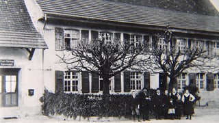 Schwarzweiss-Foto eines Landgasthofes, mit Personen im Vordergrund.