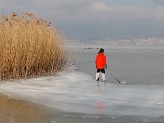 Ein Kind steht mit Schlittschuhen und Hockeyschläger auf dem gefrorenen See.