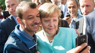 Merkel posiert mit Flüchtling für ein Selfie.