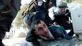 Ein arabischer Mann wird von der Polizei zu Boden gedrückt.