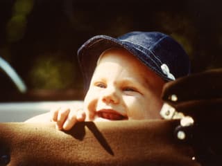 Ein Kleinkind mit blauem Sonnenhut blickt neugierig aus einem Kinderwagen.