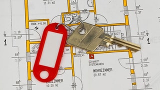 Ein Wohnungsschlüssel mit rotem Anhänger liegt auf einem Wohnungsplan.