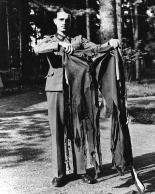 Ein Soldat auf einer Waldstrasse hält eine zerfetzte Hose in die Kamera.