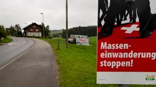 Plakat «Masseneinwanderung stoppen», dahinter Wiese, Strasse und ein Haus. Plakat «Masseneinwanderung stoppen», dahinter Wiese, Strasse und ein Haus.