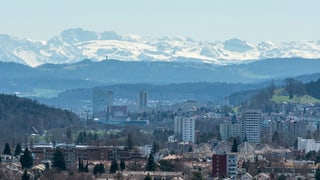 Blick auf eine Stadt, dahinter Hügel und Berge. 