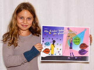 Ein Mädchen mit langen, blonden Haaren hält ein buntes Plakat in die Kamera und lächelt.
