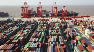 Auf dem Bild sind hunderte farbige Container zu sehen. Im Hintergrund ein Frachtschiff.