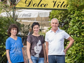 Eine ältere und eine jüngere Frau und ein Mann stehen vor dem Eingang eines italienischen Restaurants. Eine ältere und eine jüngere Frau und ein Mann stehen vor dem Eingang eines italienischen Restaurants.