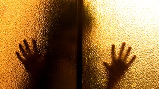 Eine dunkle Silhouette vor einem gelb beleuchteten Fensterglas. 
