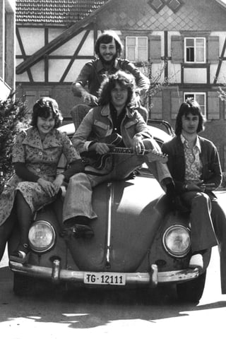 vier Männer in rockiger Aufmachung sitzen auf einem VW Käfer.