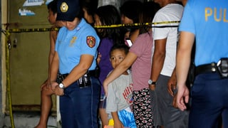 Eine Polizistin, rechts von ihr ein Junge hinter einer Absperrungsbanderole und andere Schaulustige.