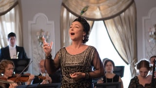 Marguerite singt mit Leidenschaft, im Hintergrund spielt ein Orchester.