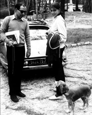 Jean Luc Godard und seine damalige Frau Anne Wiazemsky stehen vor einem Auto und schauen einen Hund an.