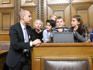 Joël Thüring steht neben den kindern, die an seinem Platz sitzen.