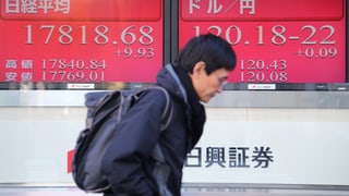 Mann geht an einer elektronischen Anzeigetafel für die Börse in Tokyo vorbei Mann geht an einer elektronischen Anzeigetafel für die Börse in Tokyo vorbei