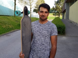 Omid hält sein Longboard in der Hand.