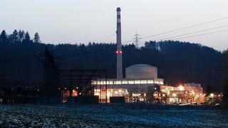 Zu sehen ist das Kernkraftwerk Mühleberg in der Dämmerung. Die Fenster sind hell erleuchtet. 