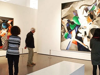 Ausstellungsraum mit Gemälden und Zuschauern.