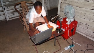 Schulmädchen arbeitet an Computer, betriebne von einem roten Power-Blox-Würfel Schulmädchen arbeitet an Computer, betriebne von einem roten Power-Blox-Würfel