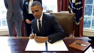 Barack Obama unterzeichnet an einem Schreibtisch ein Dekret.
