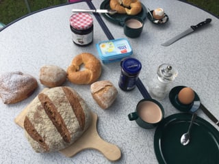Campingtisch voller Brötchen, Kaffeetasse mit Kaffe, Salz, Eier, Konfitüre. Alles eher ungeordnet.