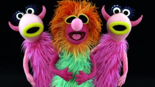 Drei haarige Muppets in einer Reihe. Sie singen.