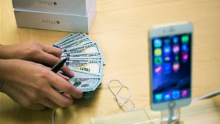 Iphone im Vordergrund, ein Apple-Mitarbeiter zählt Geld.