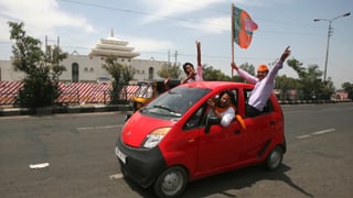 rotes Auto, in dem Männer sitzen und vor Freude die indische Flagge schwenken und die Arme rausstrecken. 