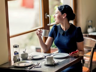 Eine Frau mit einem Smartphone an einem Kaffeetisch.