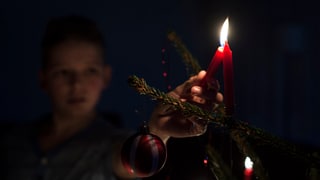 Ein Kind zündet eine Kerze an einem Weihnachtsbaum an.