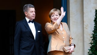 Angela Merkel winkt im Abendkleid neben seinem Ehemann Joachim Sauer.