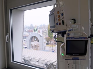 Ein Überwachungsgerät in einem Aufwachraum; daneben ein Fenster mit Blick auf den Torbogen vor dem Luzerner Bahnhof.