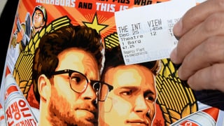 Filmplakat von «The Interview» und jemand, der ein Kinoticket davor hält.