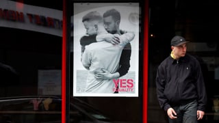 Zwei sich umarmende Männer auf einem Yes-Plakat. Daneben steht ein Mann, der wegschaut.