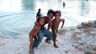 Drei Kinder stehen am Strand und schauen in die Kamera.