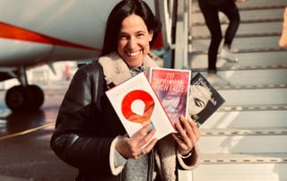 Annette König ist kurz davor in ein Flugzeug zu steigen. In der Hand hält sie drei Romane, die im Iran spielen. 