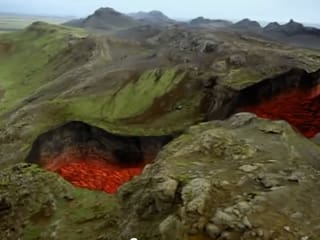 Eine gebirgslandschaft, in der sich ein rieisger Graben auftut, durch den Lava fliesst.