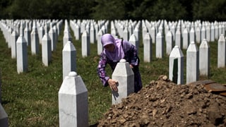 Eine muslimische Frau pflegt einen Grabstein auf einem Friedhof.