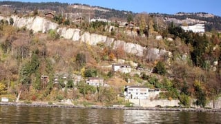 Blick vom Vierwaldstättersee auf ein Felsband. Darunter stehen mehrere Häuser.