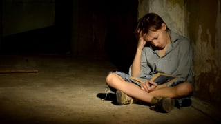 Kind sitzt in dunklem Keller und liest