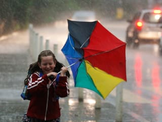 Ein Schulkind kämpft sich durch den strömenden Regen. Der Schirm wurde vom Wind umgestülpt.