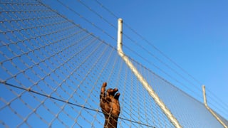 Hand eines afrikanischen Migranten, Zaun festhaltend
