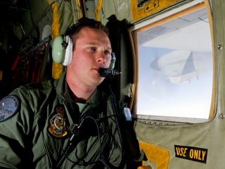 Ein Mann mit Kopfhörern sitzt an einem Fenster in einer Militärmaschine