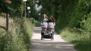 zwei Frauen stossen draussen einen Kinderwagen