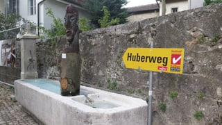Wegweiser «Huberweg», im Hintergrund Holzskulptur.