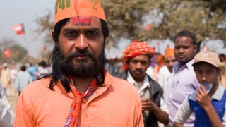 Im Vordergrund junger indischer Mann, orange gekleidet. Im Hintergrund andere junge Männer  