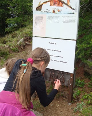 Zwei Mädchen knien bei einem Spielposten auf der Wanderung.