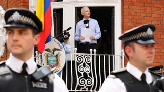 Julian Assange auf dem Balkon der Botschaft Ecuadors in London, im Vordergrund Polizisten.