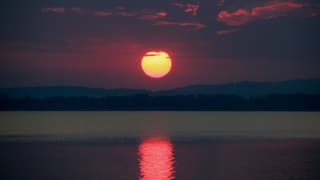 Sonnenaufgang am Murtensee mit rotspiegelnder Sonne auf dem See