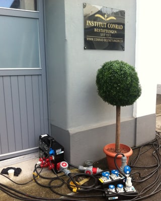 Eingang zu einem Inbdustriegebäude, neben der Tür ein Schild "Institut Conrad", am Boden viele Kabel.